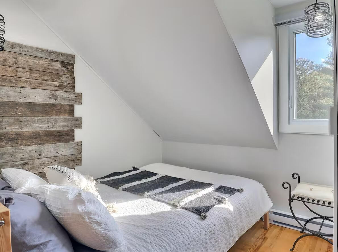 Cozy minimalist bedroom with rustic wood accent wall, sloped ceiling, and natural light from window