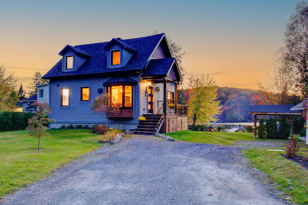 Cozy lakeside chalet on Lake Lovering with warm interior lights, surrounded by autumn trees and a peaceful waterfront at sunset