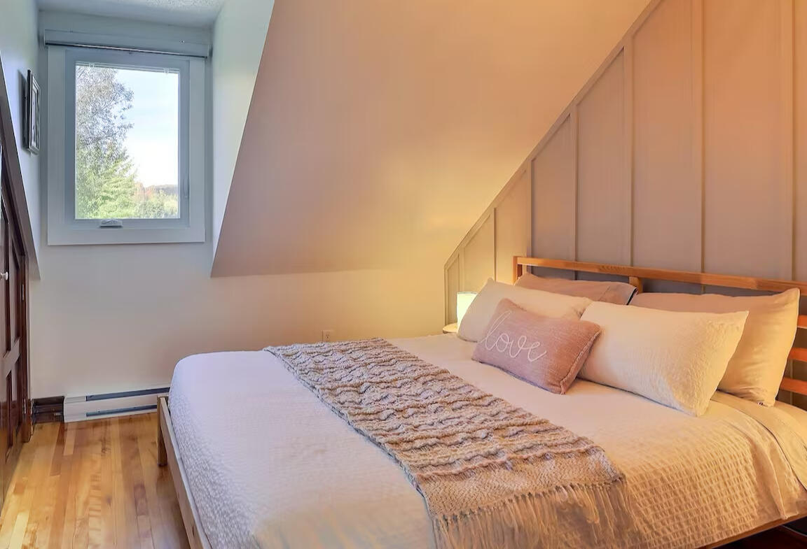 Cozy attic bedroom with warm lighting and peaceful ambiance Warm and cozy attic bedroom with a comfortable bed, soft lighting, and a window with forest view