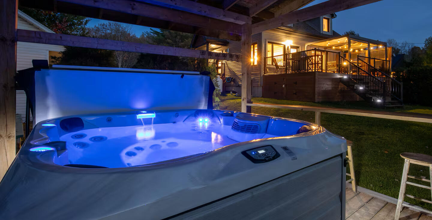 Private outdoor hot tub at Lake Lovering chalet with blue lighting, overlooking a cozy illuminated terrace at night