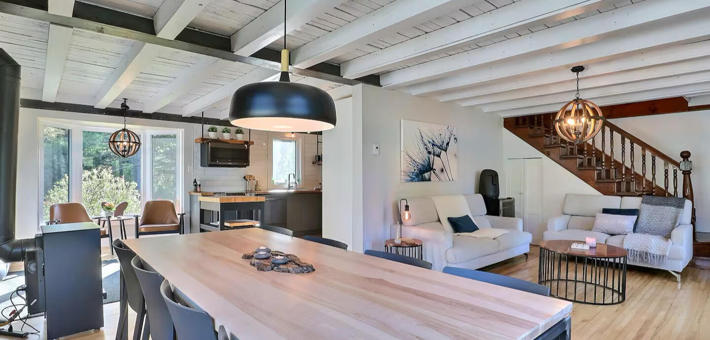 Open-concept living space at Chalet Le Monarque near Magog, featuring the living room, dining area, and modern kitchen. Bright living and dining area at Chalet Le Monarque near Magog, featuring an open kitchen and a large wooden table for 8 people.
